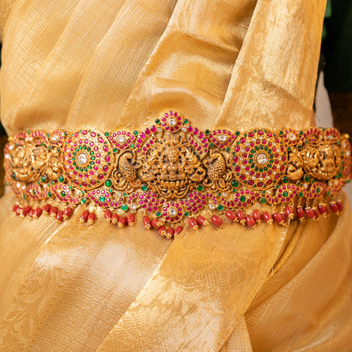 Decorative gold belt with red and green stones on a gold fabric background