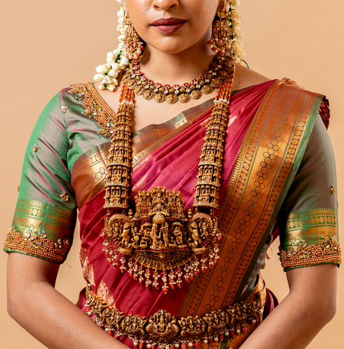 A woman wearing a traditional saree with gold-plated silver jewelry on a beige background